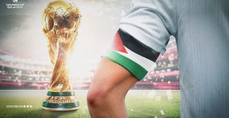 Arm of soccer player with a Palestine flag armband and nearby is a by World Cup trophy.