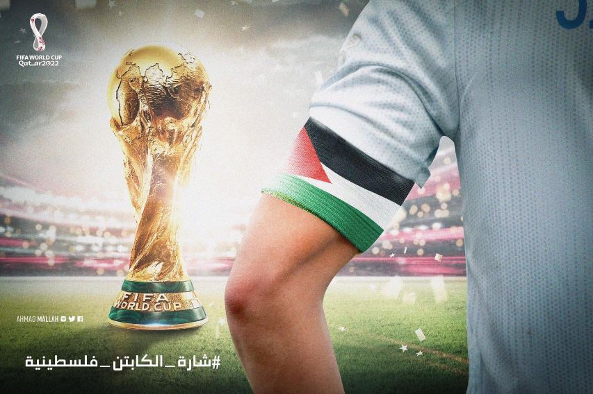 Arm of soccer player with a Palestine flag armband and nearby is a by World Cup trophy.
