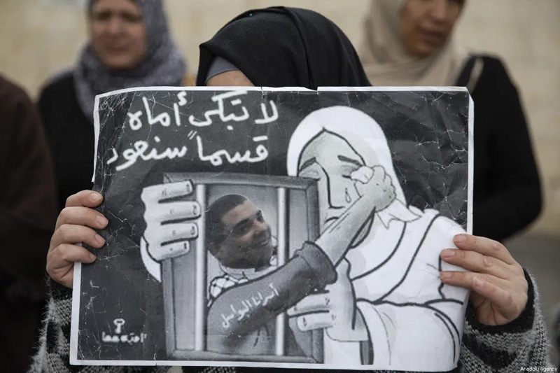Woman holding poster depicting imprisoned man wiping away mother's tears.