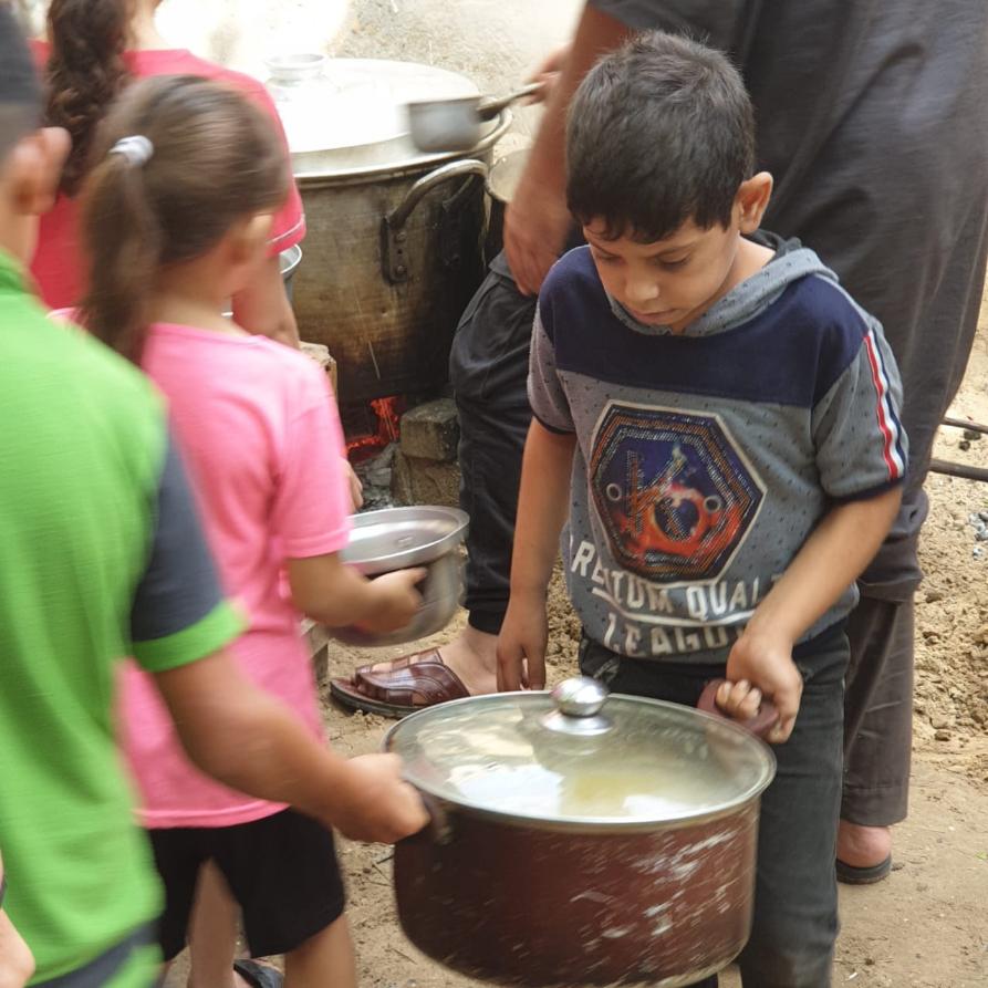 Boy carrying pot of food at Gaza food distribution center.