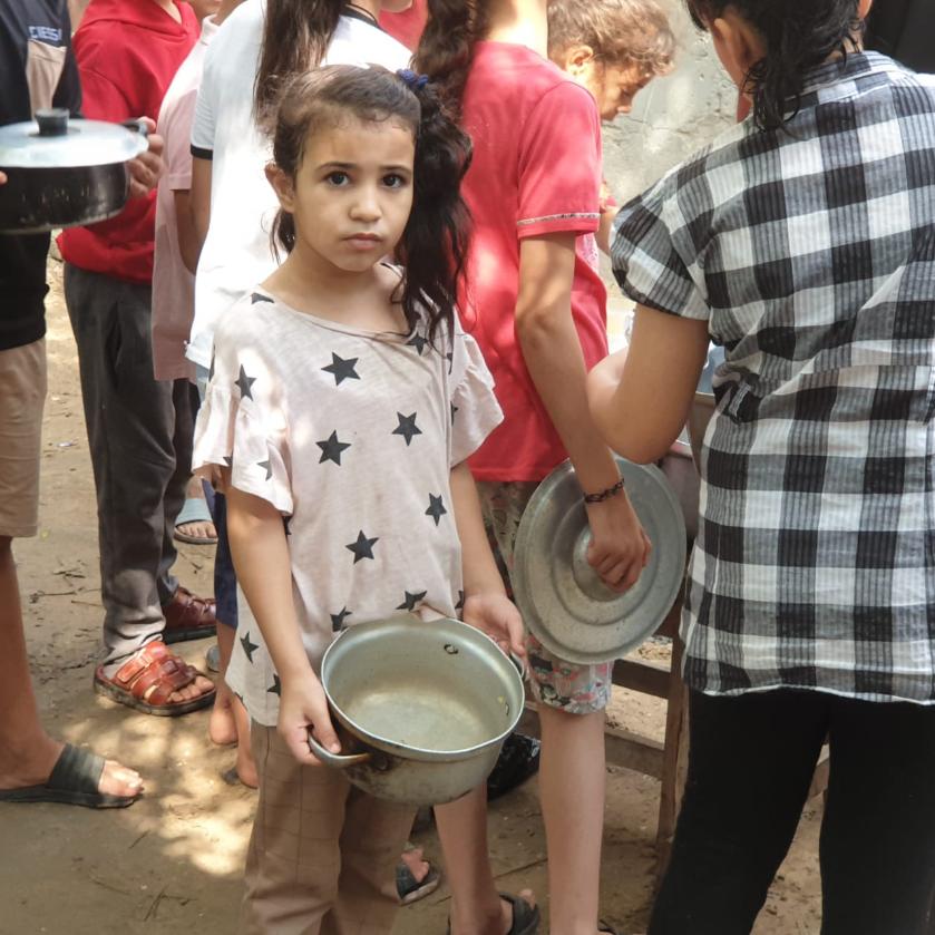 Little girl holding empty pot at Gaza food distribution program.