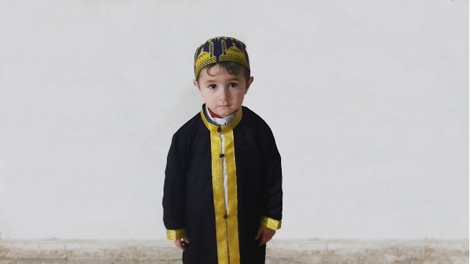 3-year-old boy in gold and purple traditional cap and robe.