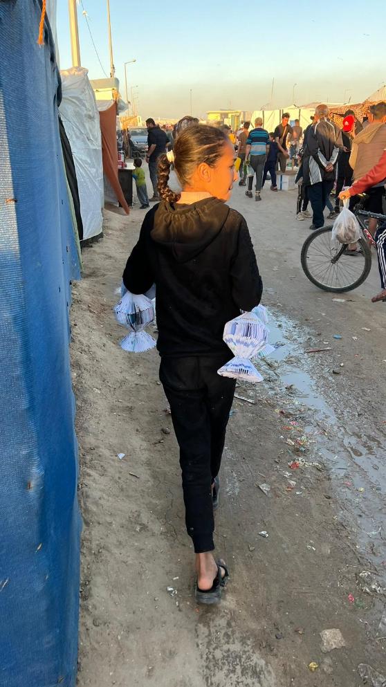 Girl in Rafah displacement camp carrying paper lanterns.