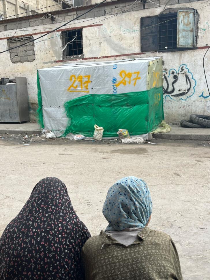 Two women sitting in front of tents on street in Rafah.