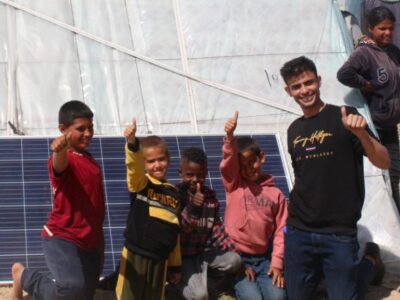 Children and young adult standing by solar panel and tent in Gaza.