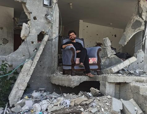 Momen Alsammak, sitting on upholstered chair among the rubble of his home.