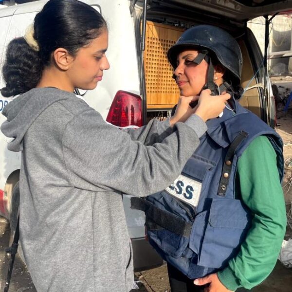 A young adult daughter adjusting the helmet on her mother, who is wearing a PRESS vest.