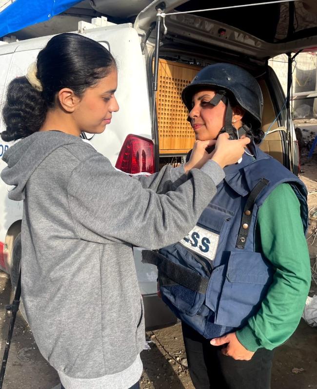 A young adult daughter adjusting the helmet on her mother, who is wearing a PRESS vest.