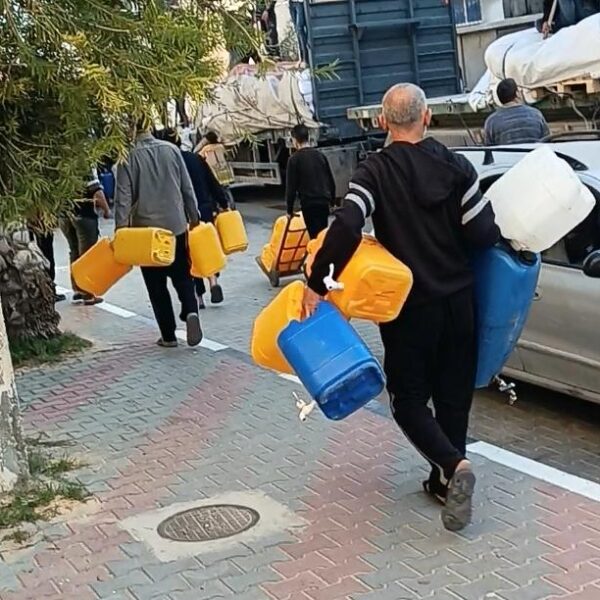 Men carrying water jugs walking down street.
