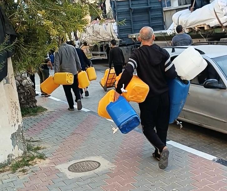 Men carrying water jugs walking down street.