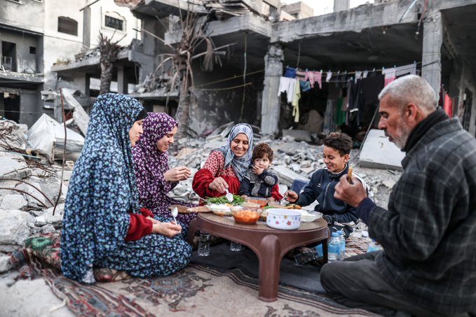 Familyl eating Iftar meal in front of destroyed building in Gaza.