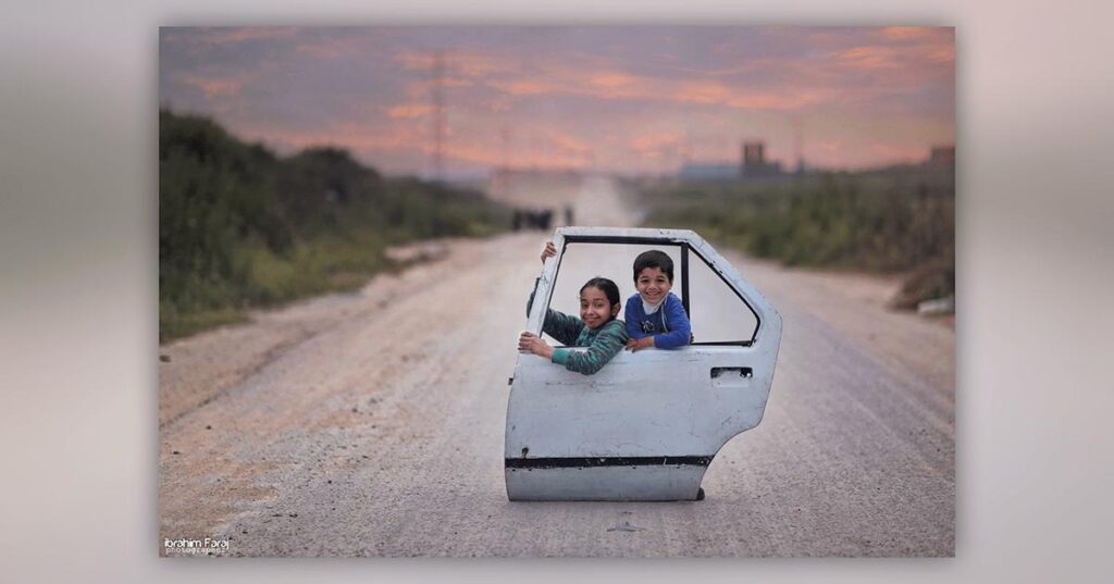 Two children playing with a car door in an empty road.