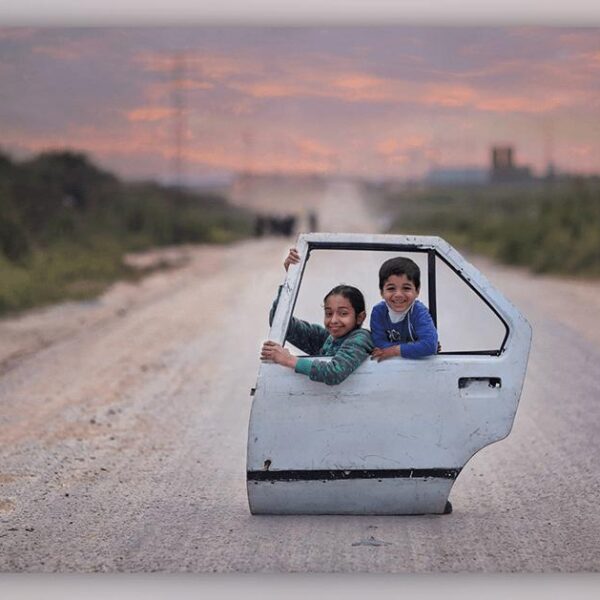 Two children playing with a car door in an empty road.