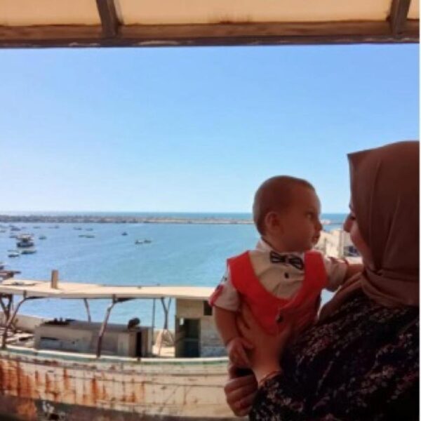 Mother with child by sea in front of moored boat.