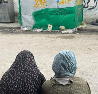 Two women in hijab looking at a sidewalk tent in Rafah.