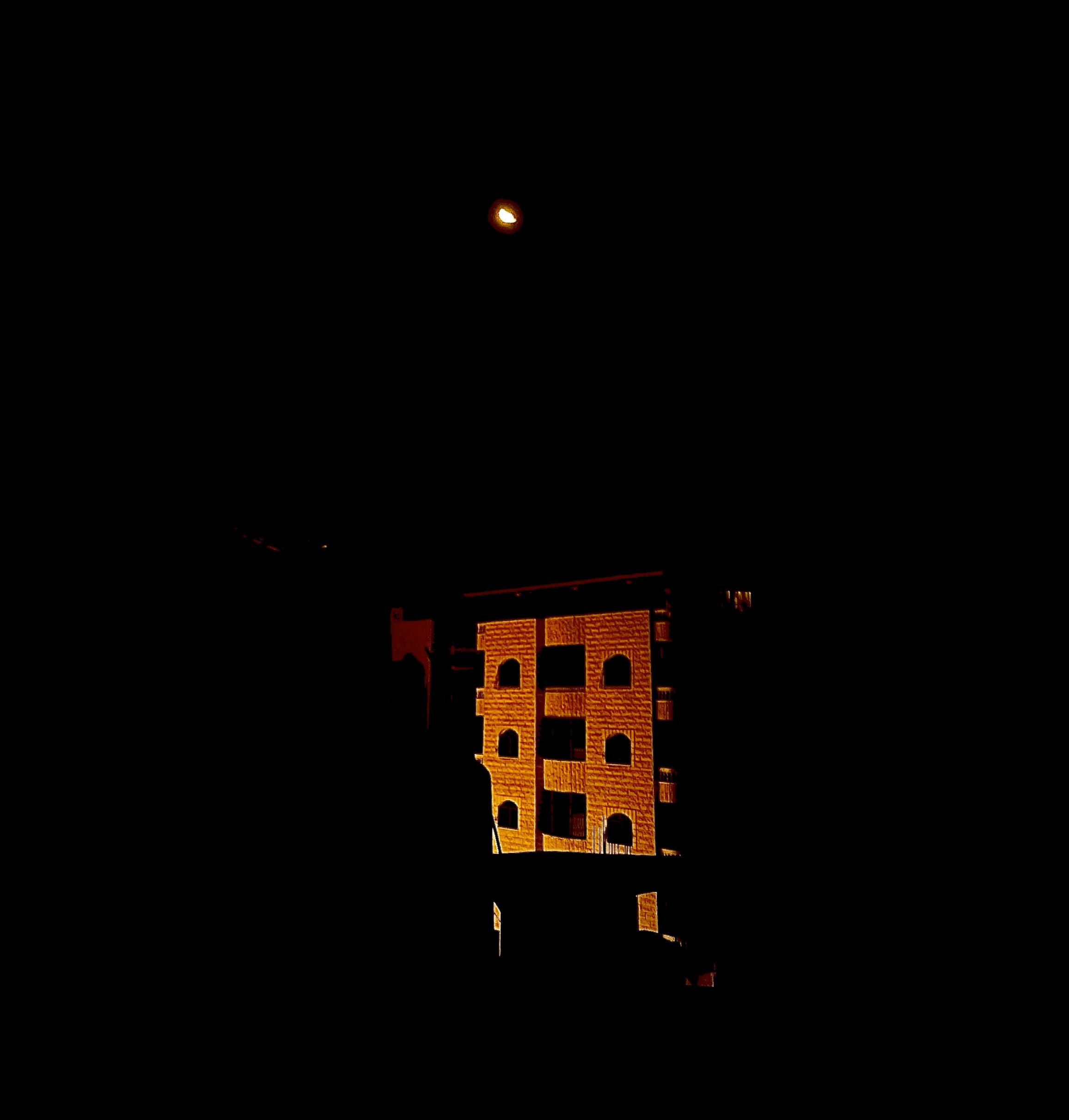 Apartment building in the nighttime, with moon above.