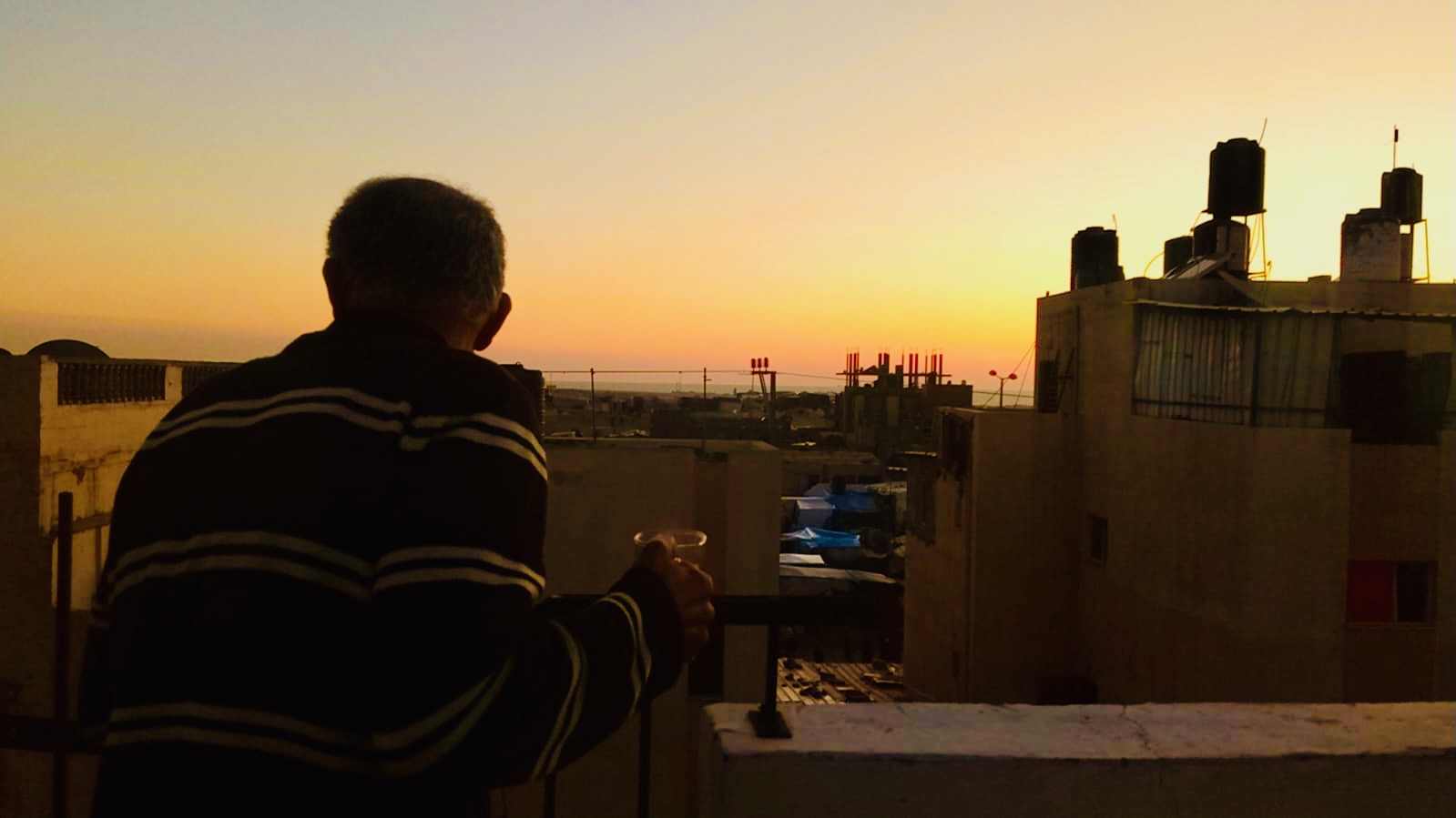 A father on the balcony in Gaza, looking at the sunset.