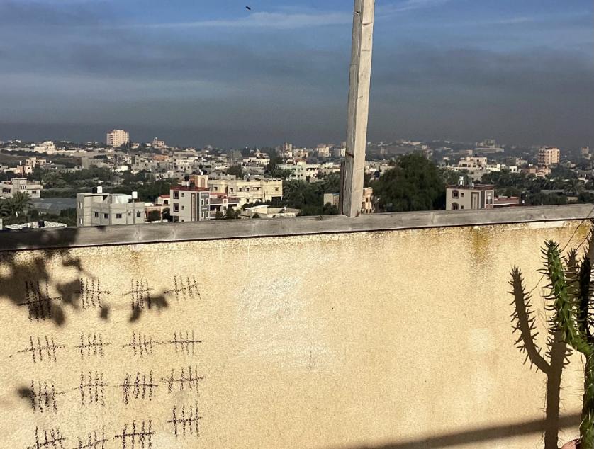 Smoke in the sky of Gaza City and in the foreground where the days of war are recorded with hatchmarks on the balcony wall.