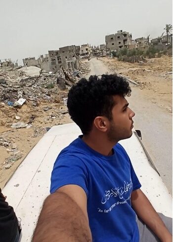Young man in back of jeep riding through a destroyed neighborhood in Gaza.