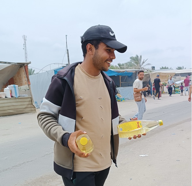 Young man with two bottles of oil in his hands standing on a street in Khan Younis.