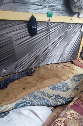 Inside a tent; blankets lay on a dirt floor that is muddy.