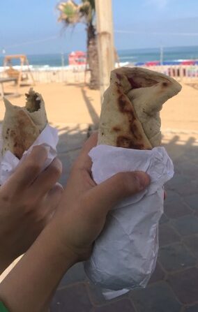 GTwo hands holding falafel sandwiches n front of the Gaza sea.