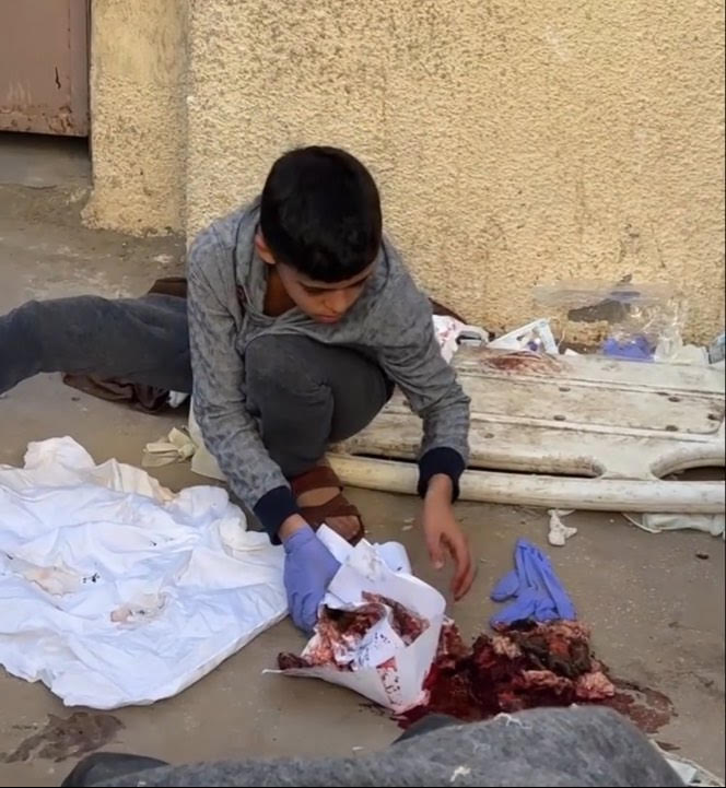 Young child putting onto a white sheet the body parts of a family member killed in an Israeli airstrike.