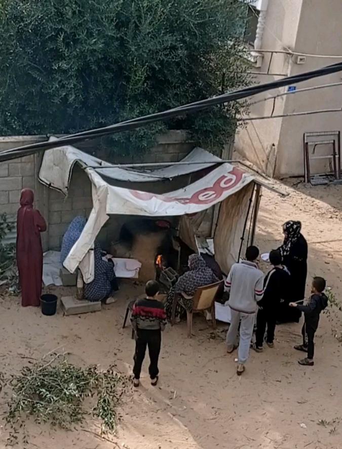People standing around clay oven beneath a loose tent in Gaza.